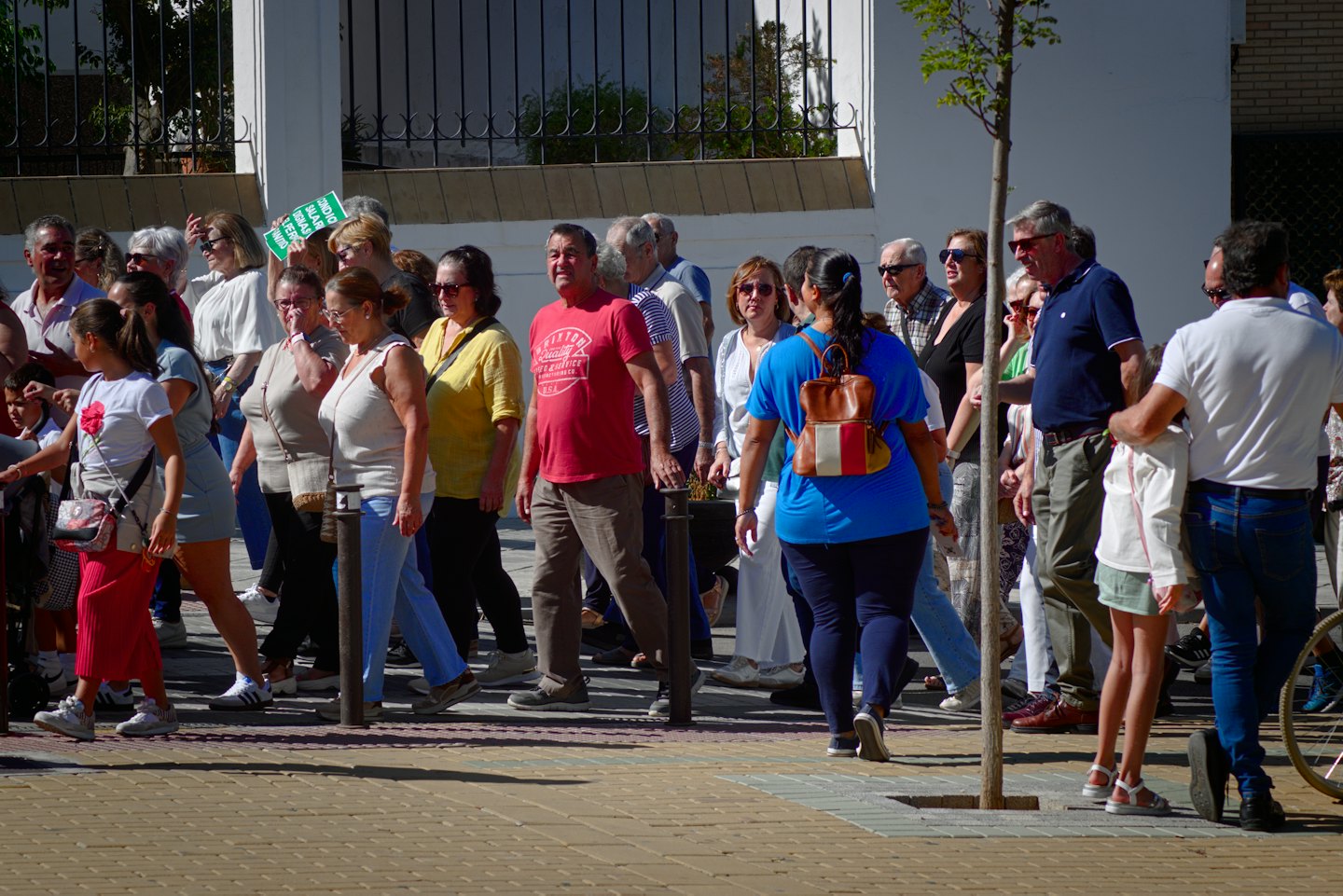 Persone camminano in una piazza con un cartello verde.