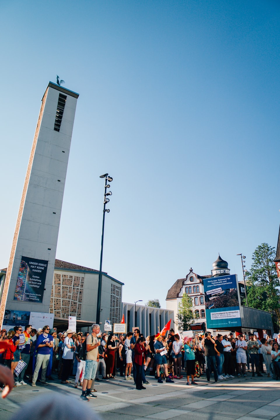 Folla eterogenea riunita in una piazza cittadina soleggiata durante un evento all'aperto.